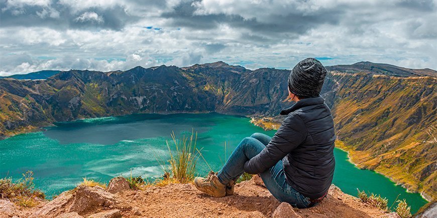 Kvinde sidder på kanten af kratersøen Quilotoa i Ecuador.