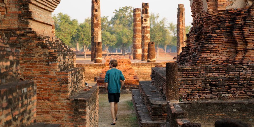 Mand går ved ruinerne i Sukhothai ved solopgang